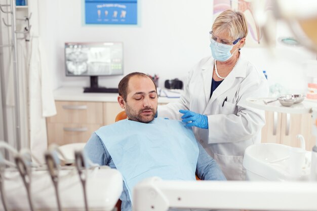 Senior stomatologist helping patient to stand up after dental surgery during medical stomatology clinic office