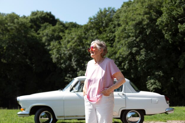 Senior traveler wearing red sunglasses next to her car