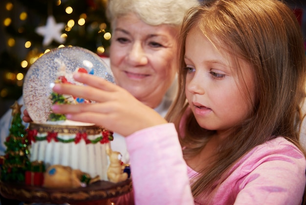 Senior with girl watching christmas snow globe
