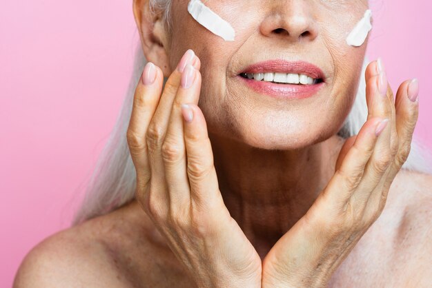 Senior woman applying skin care on face