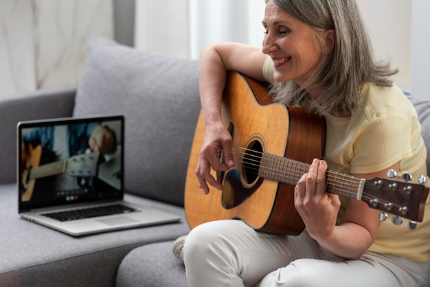 自宅​の​ソファ​で​ノート​パソコン​を​使って​ギター​の​レッスン​を​する​シニア​女性