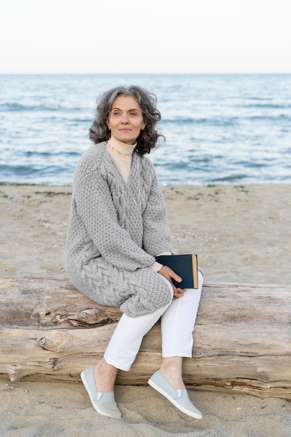 Foto gratuita senior donna in spiaggia con in mano un libro