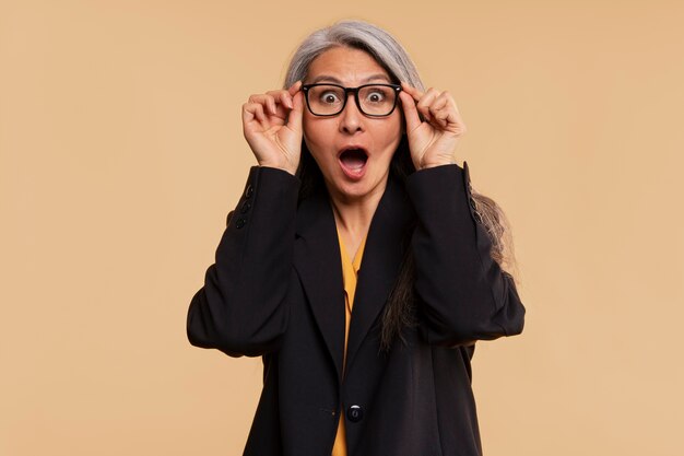 Senior woman being surprised and wearing glasses against a yellow background