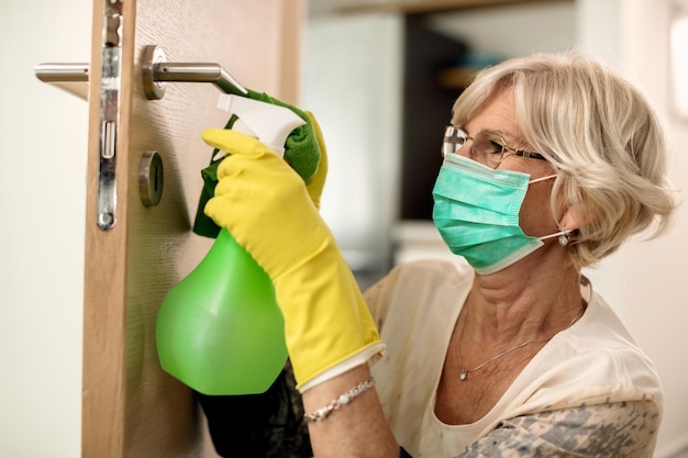 Senior woman disinfecting door handle during coronavirus pandemic