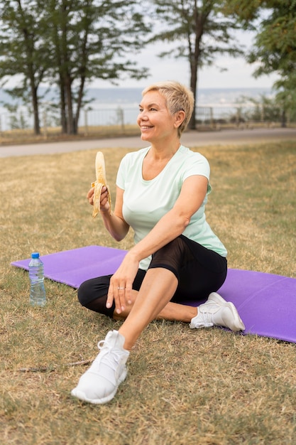ヨガの後に公園で屋外でバナナを食べる年配の女性