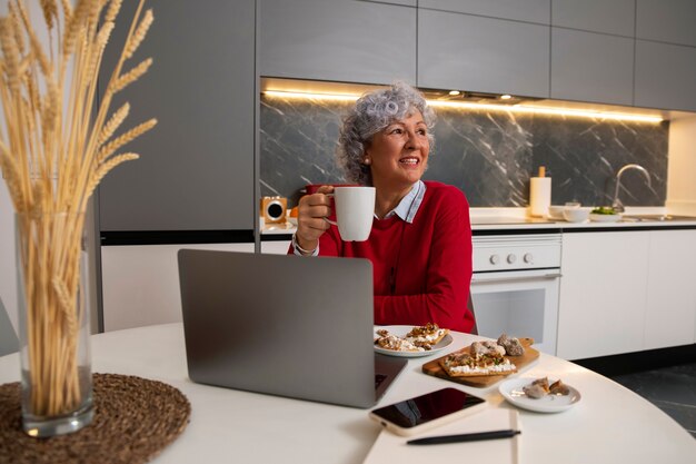 Бесплатное фото Пожилая женщина ест блюдо из инжира дома и использует ноутбук