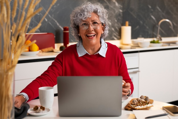 Foto gratuita donna anziana che mangia il piatto di fichi a casa e usa il computer portatile