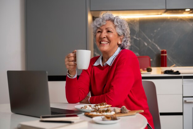 Foto gratuita donna anziana che mangia il piatto di fichi a casa e usa il computer portatile