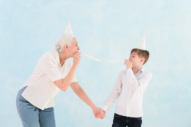 Senior woman enjoying with her grandson with party hat and horn on blue surface