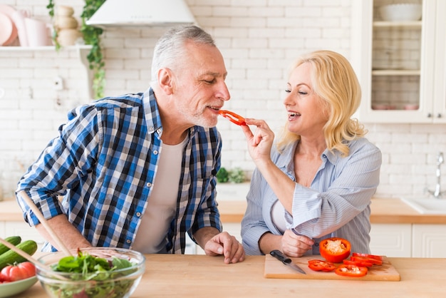 Foto gratuita donna maggiore che alimenta peperone dolce al suo marito nella cucina