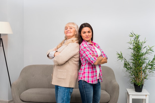 Senior woman and her adult daughter standing back to back at home