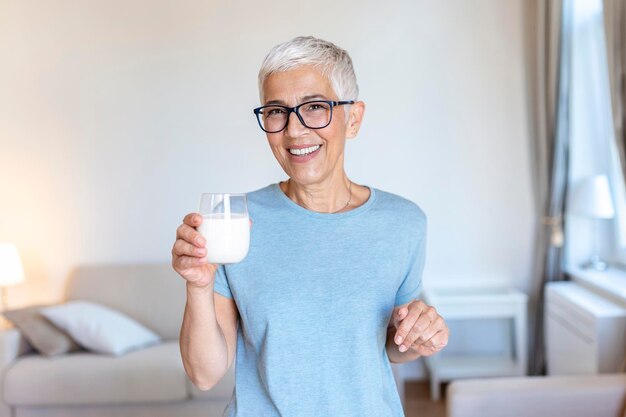 Senior Woman Holding Glass Of Milk At Home Middle age woman drinking a glass of fresh milk with a happy face standing and smiling with a confident smile showing teeth
