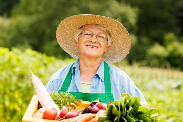 野菜と木箱を保持している年配の女性