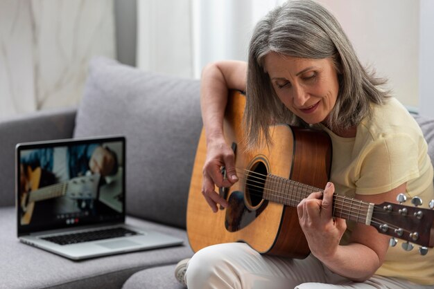 Senior woman at home on the couch using laptop for guitar lessons