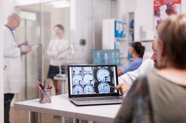 診断について医師と話し合っている間、脳のct-scanを見ている病院のオフィスの年配の女性。クリニックの廊下で白髪の病気の若い女性と年配の医者。