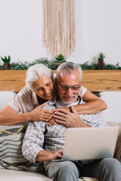 Donna maggiore che abbraccia il suo marito che per mezzo del computer portatile