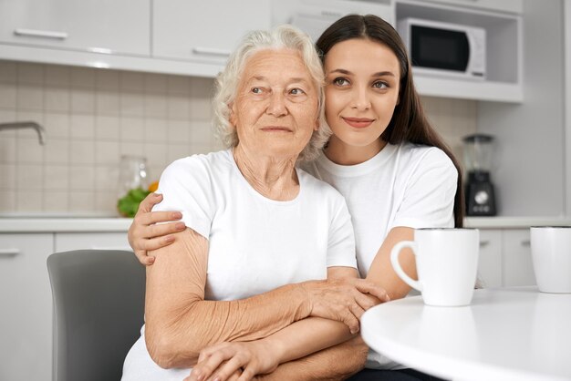 Старшая женщина обнимается с внучкой на кухне