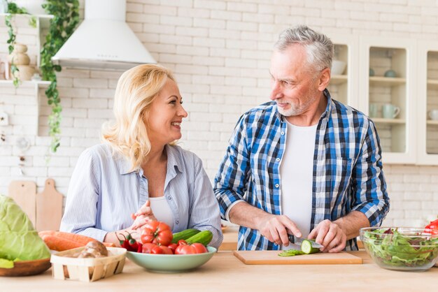 Senior woman looking at her husband cutting the slice of cucumber with knife