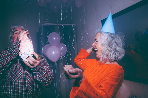 年配の女性が誕生日パーティーでシャンパンのボトルを飲む彼女の夫を見て