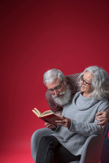 赤い背景の本を見て彼女の夫を見ている年配の女性