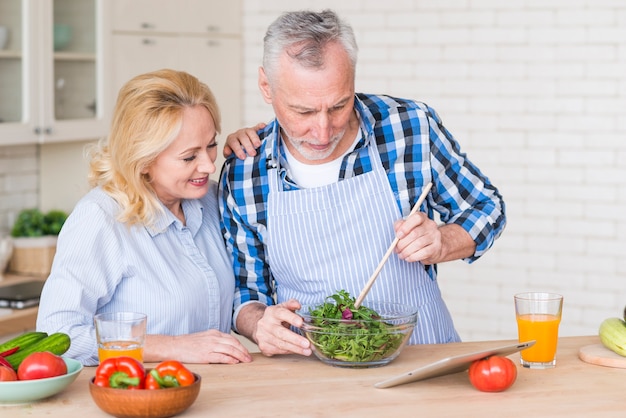 Donna maggiore che esamina suo marito che prepara l'insalata verde che esamina compressa digitale