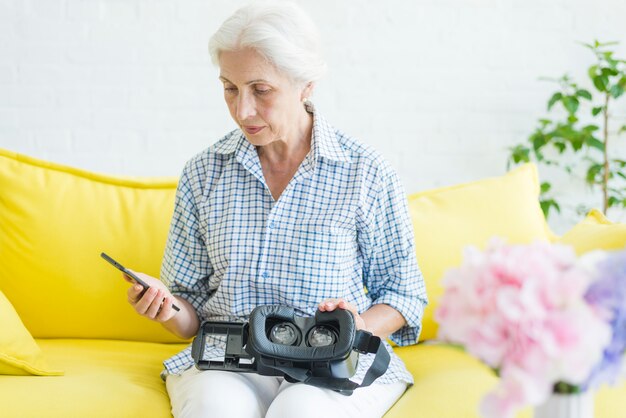 Donna maggiore che esamina telefono cellulare con la macchina fotografica virtuale