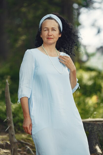 Senior woman looks at the camera. Lady in a blue dress. Brunette walks.