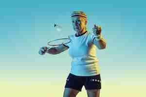 無料写真 ネオン光のグラデーションの背景にスポーツウェアでバドミントンをしている年配の女性
