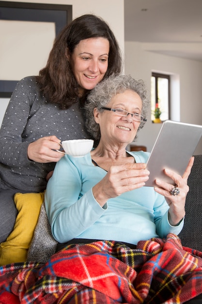 Senior woman reading online book together with adult daughter