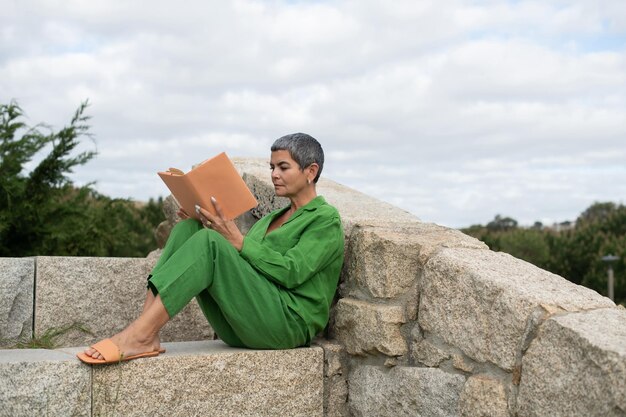 Senior woman reading in park. Female model with short grey hair in bright clothes holding book. Leisure, literature concept