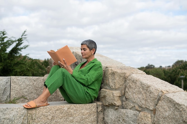 Старшая женщина читает в парке. Женская модель с короткими седыми волосами в яркой одежде держит книгу. Досуг, литературная концепция