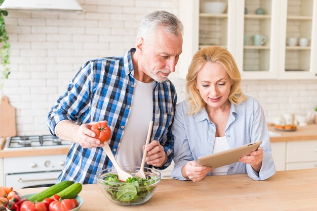 年配の女性が台所でサラダを準備する彼女の夫にレシピを示す