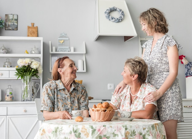 Senior woman sitting on chair looking at her daughter and grand daughter in kitchen