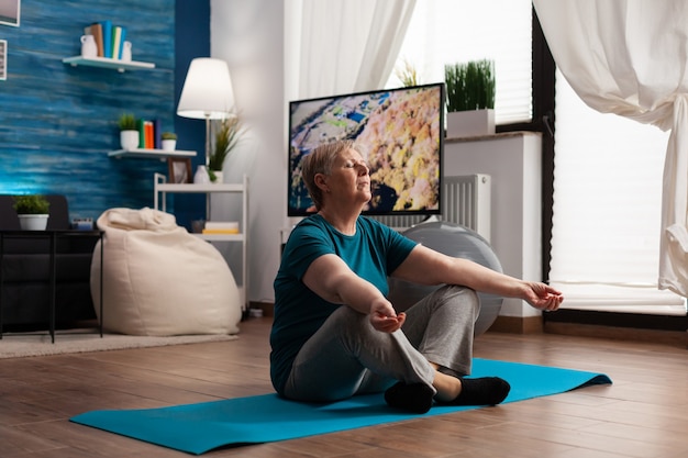 Senior woman sitting comfortable in lotus position on yoga mat with closed eyes