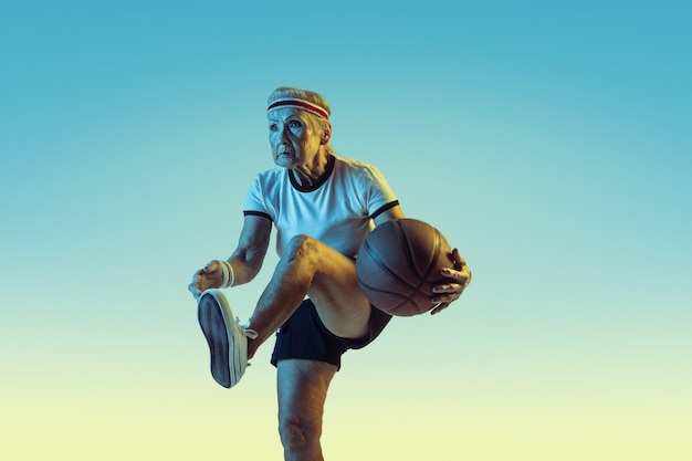 Senior woman in sportwear playing basketball on gradient