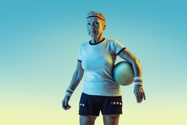 Старшая женщина в спортивной тренировке в волейбол на фоне градиента, неоновый свет. Девушка-модель в отличной форме остается активной. Понятие спорта, активности, движения, благополучия, уверенности. Copyspace.