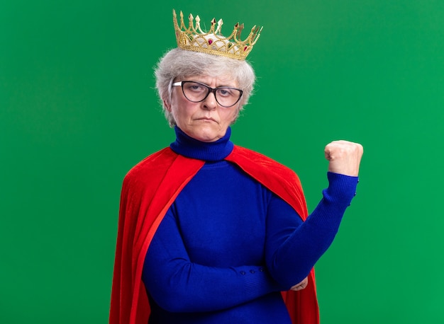 Senior woman superhero wearing red cape and glasses with crown on head looking at camera