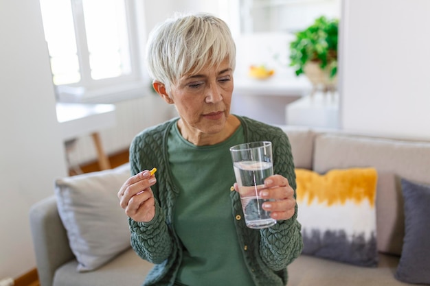 年配の女性は、手に水のガラスと錠剤を取ります