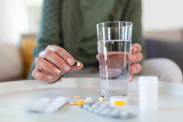 Senior woman takes pill with glass of water in hand