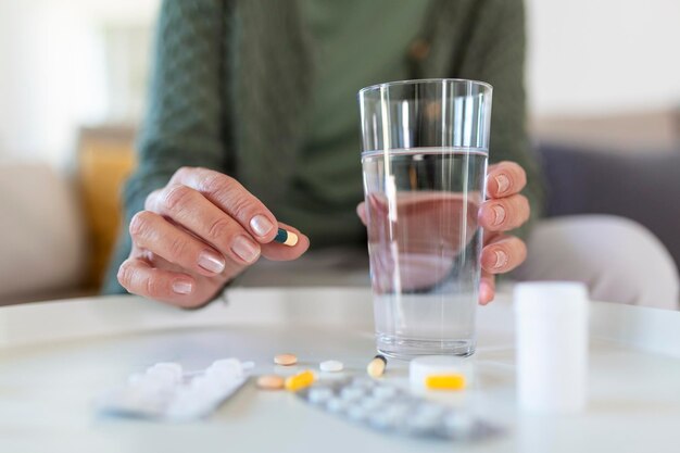 Пожилая женщина принимает таблетку со стаканом воды в руке