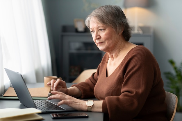 Foto gratuita senior donna che utilizza laptop seduto alla scrivania in soggiorno