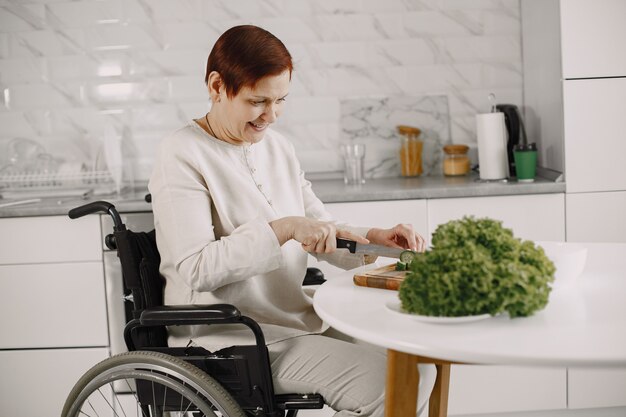 Старшая женщина в инвалидной коляске, приготовление пищи на кухне. Людей с ограниченными возможностями