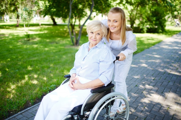 Senior woman on wheelchair with caregiver outdoors