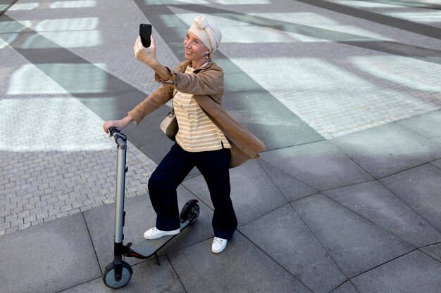 市内で電動スクーターを持って自撮りをしている年配の女性