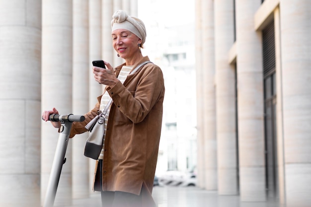 スマートフォンを使用して市内の電動スクーターを持つ年配の女性