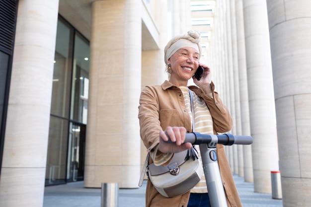 Senior donna con uno scooter elettrico parlando al telefono in città