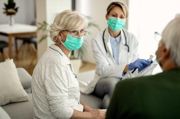 Senior woman with face mask talking to her husband during doctor's home visit
