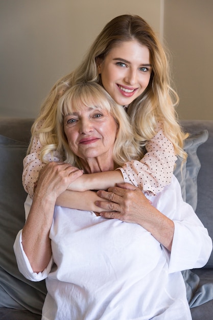 Senior woman with granddaughter or daughter hugging on couch