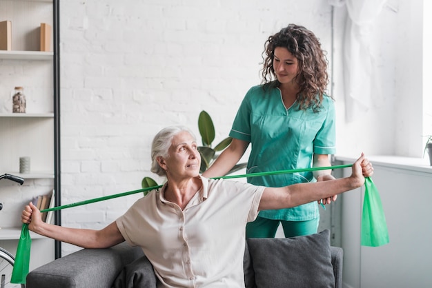 Senior woman with stretch band being assist by female physiotherapist