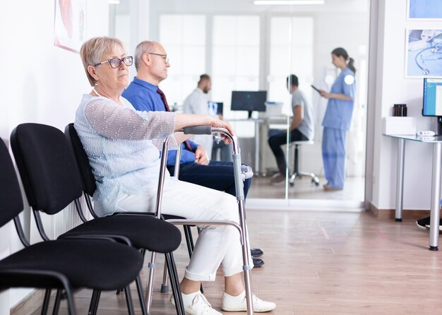 Senior woman with walking frame in hospital waiting room for rehabilitation treatment